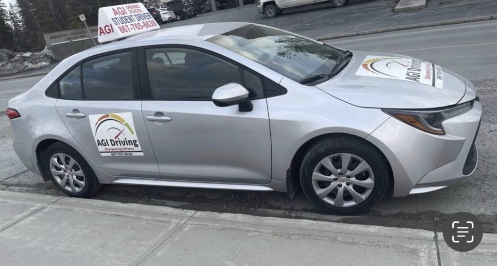 agi-driving-silver-car-parked-on-street-with-signage