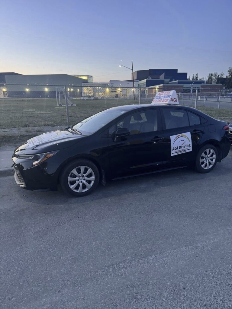 black car with agi driving sign in parking lot at sunset